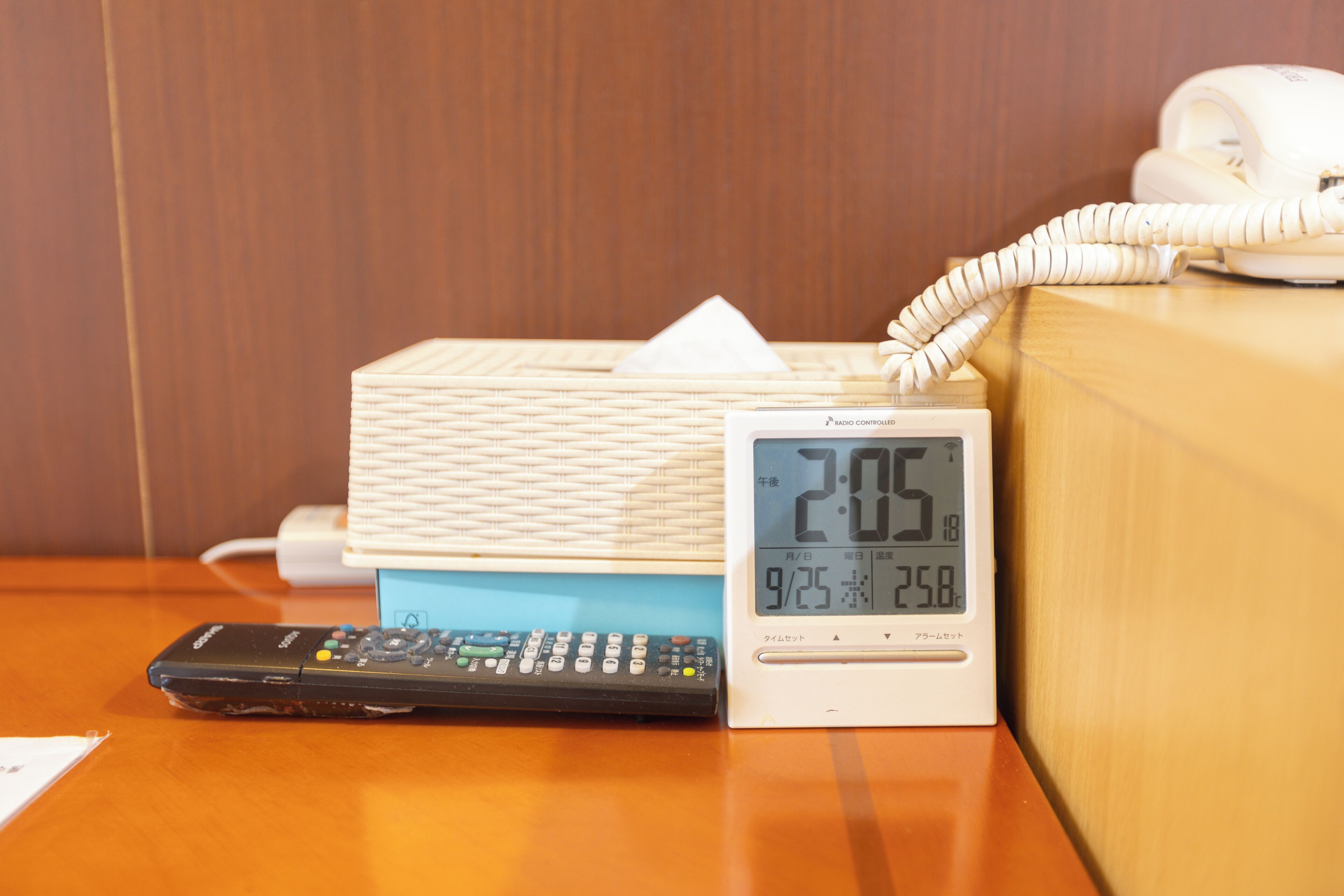 A bedside table with a white bedside lamp, a digital clock displaying the time, and a remote control.