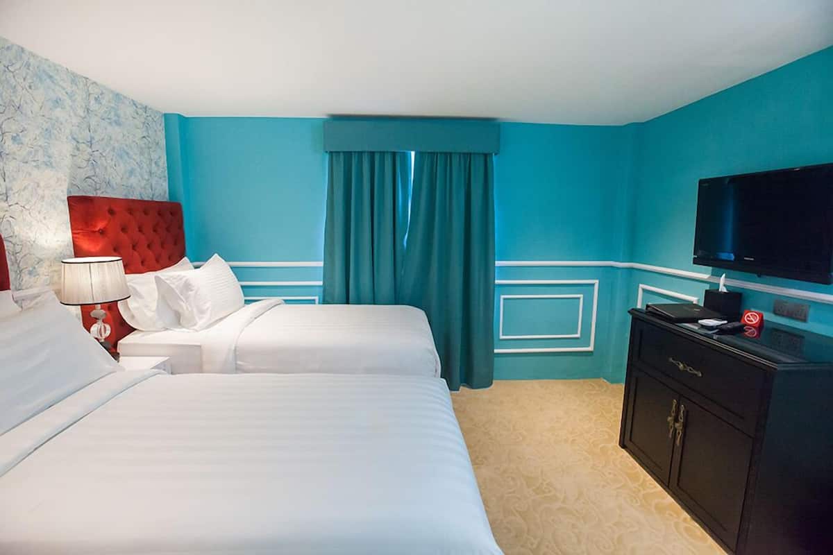 Camera d'albergo con due letti, televisione, poggiatesta rosso, tenda blu e un minibar.