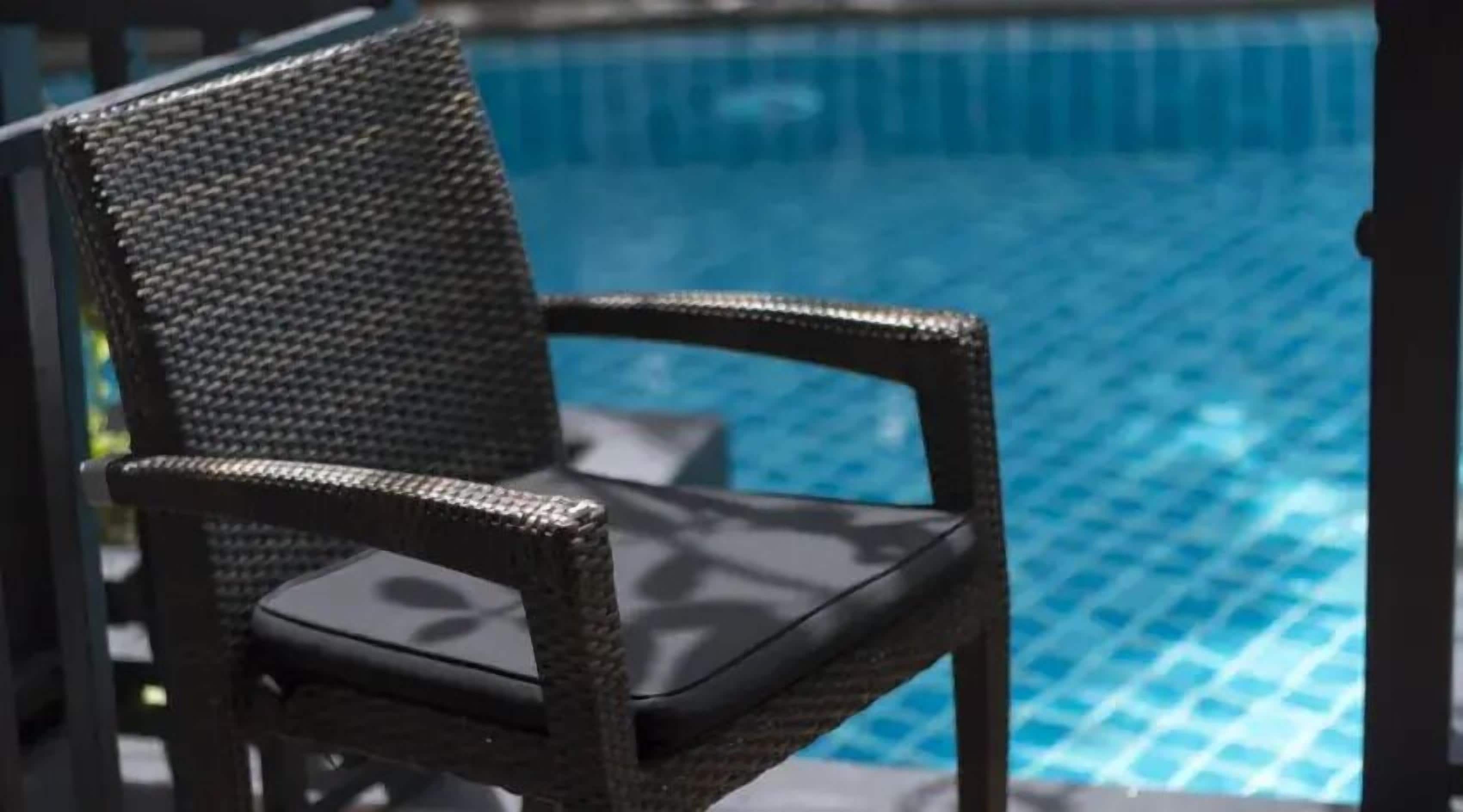 A wicker chair with a cushion by a pool.