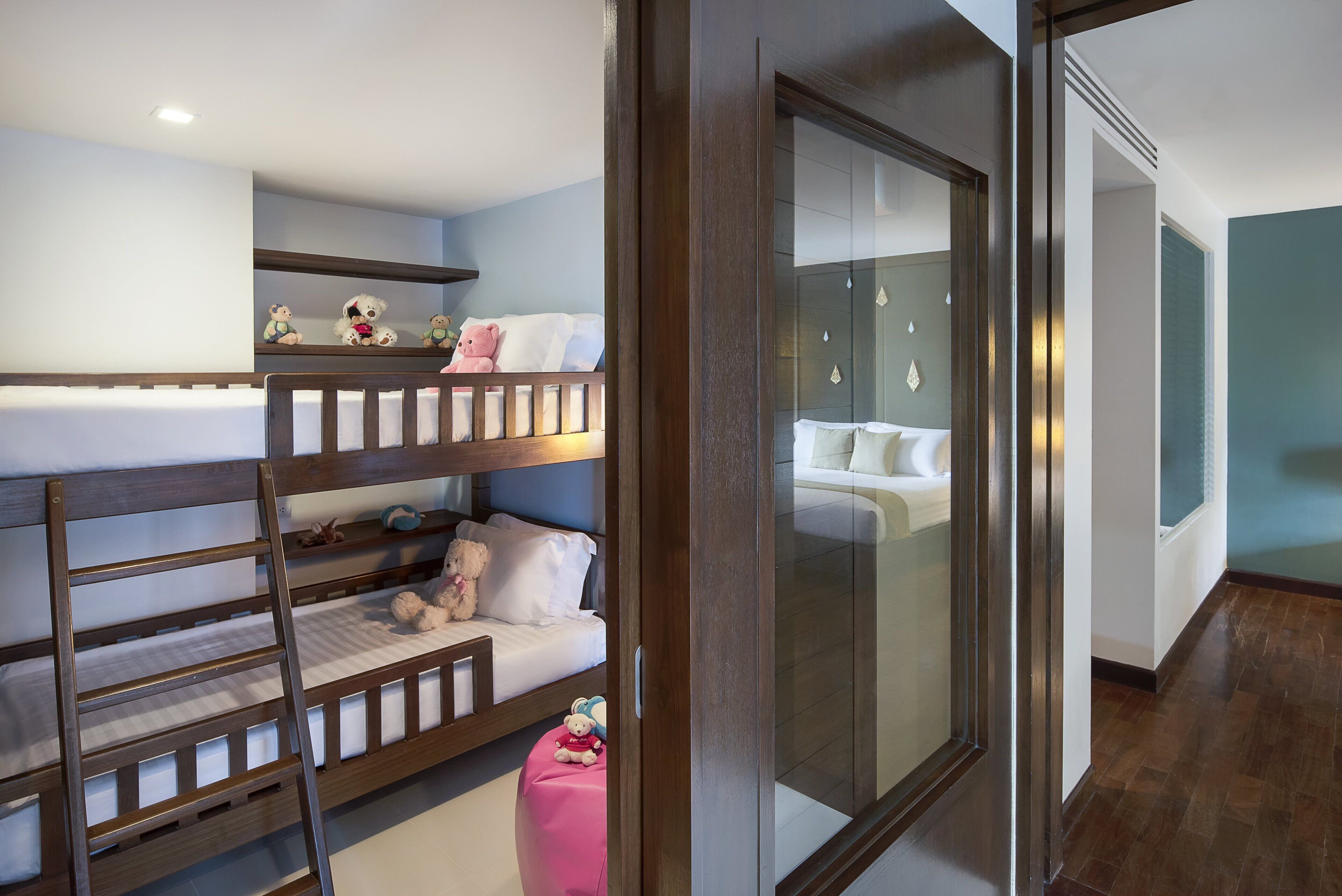 Een slaapkamer met stapelbed, een roze poef en een glazen deur naar een badkamer.