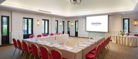 A conference room with a long table, red chairs, and a projector screen displaying 'CENTARA'.
