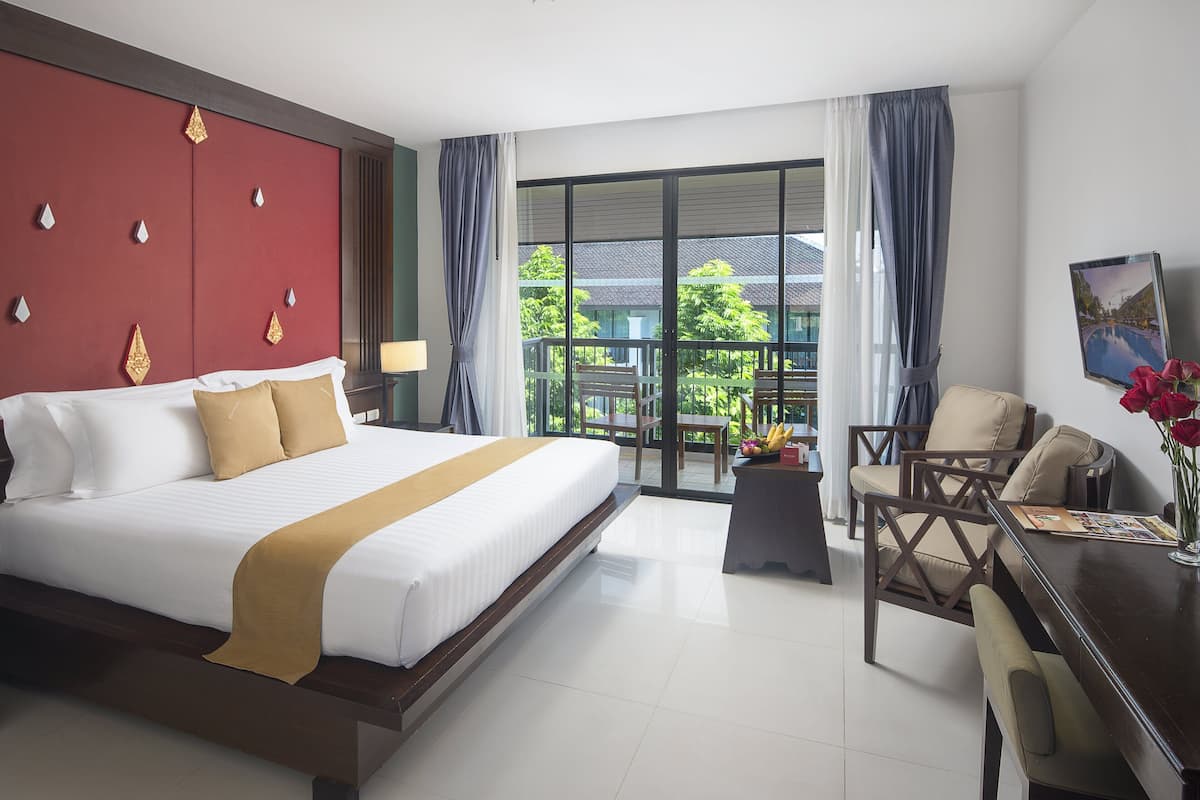 Une chambre d’hôtel dotée d’un grand lit, d’un bureau avec des chaises, d’un balcon avec une table et des chaises, et offrant une vue sur la verdure environnante.