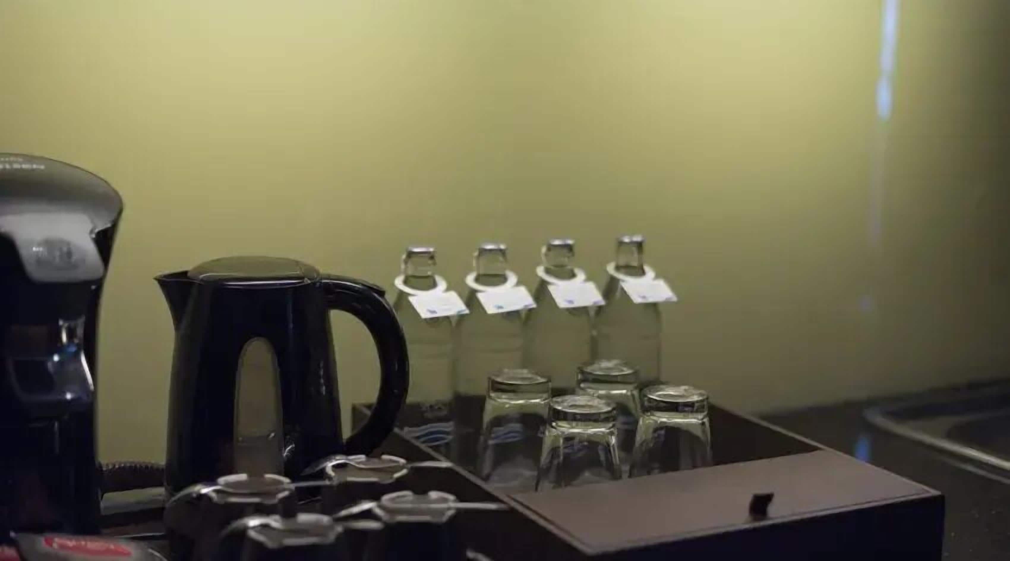 A coffee station with a coffee maker, a kettle, and several labeled bottles of water.
