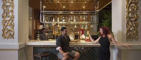 A bar area with a wooden ceiling, shelves of bottles, and a decorative wall.