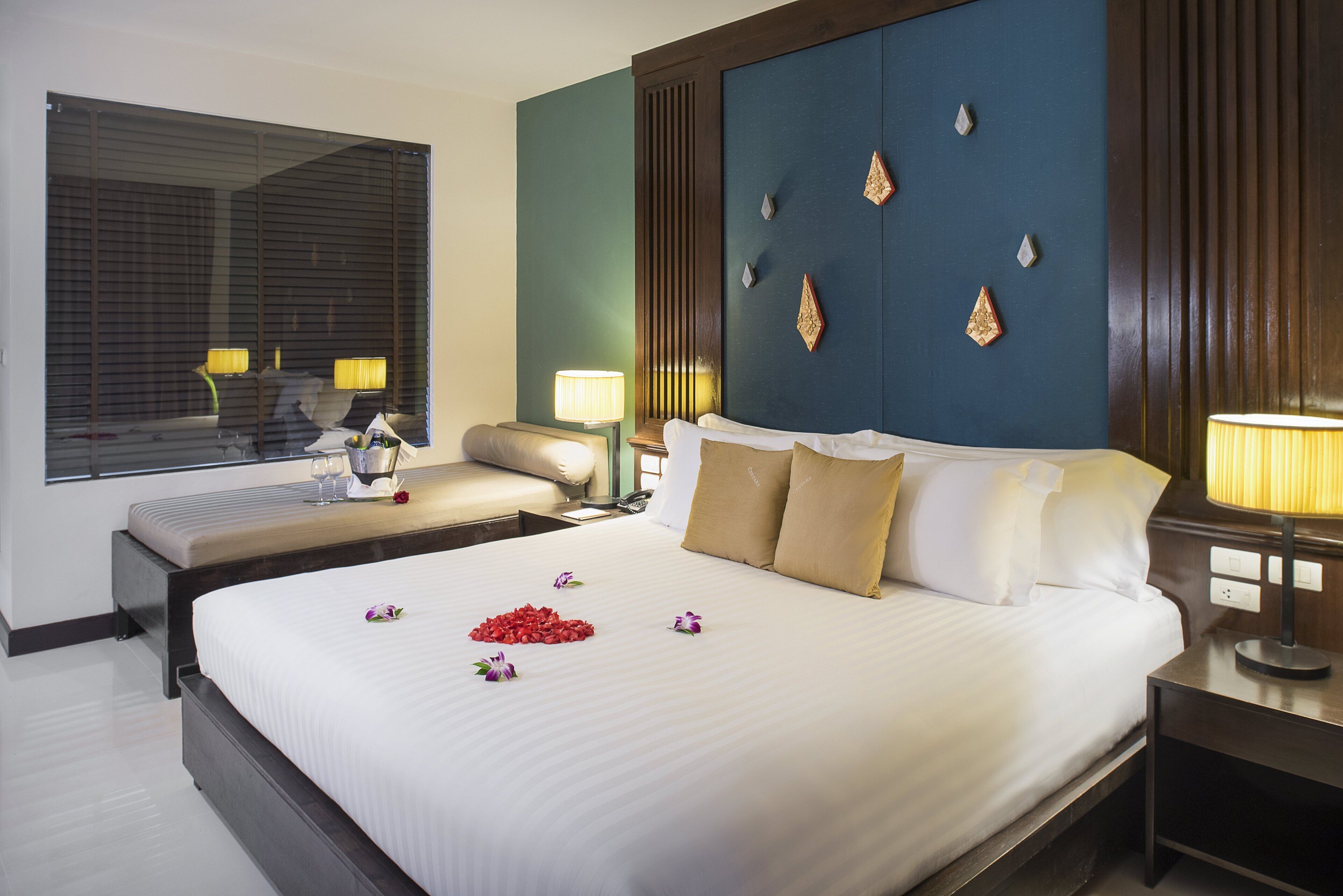 Habitación de hotel con una cama grande, lámparas de noche, una ventana con persianas y paneles decorativos en la pared.