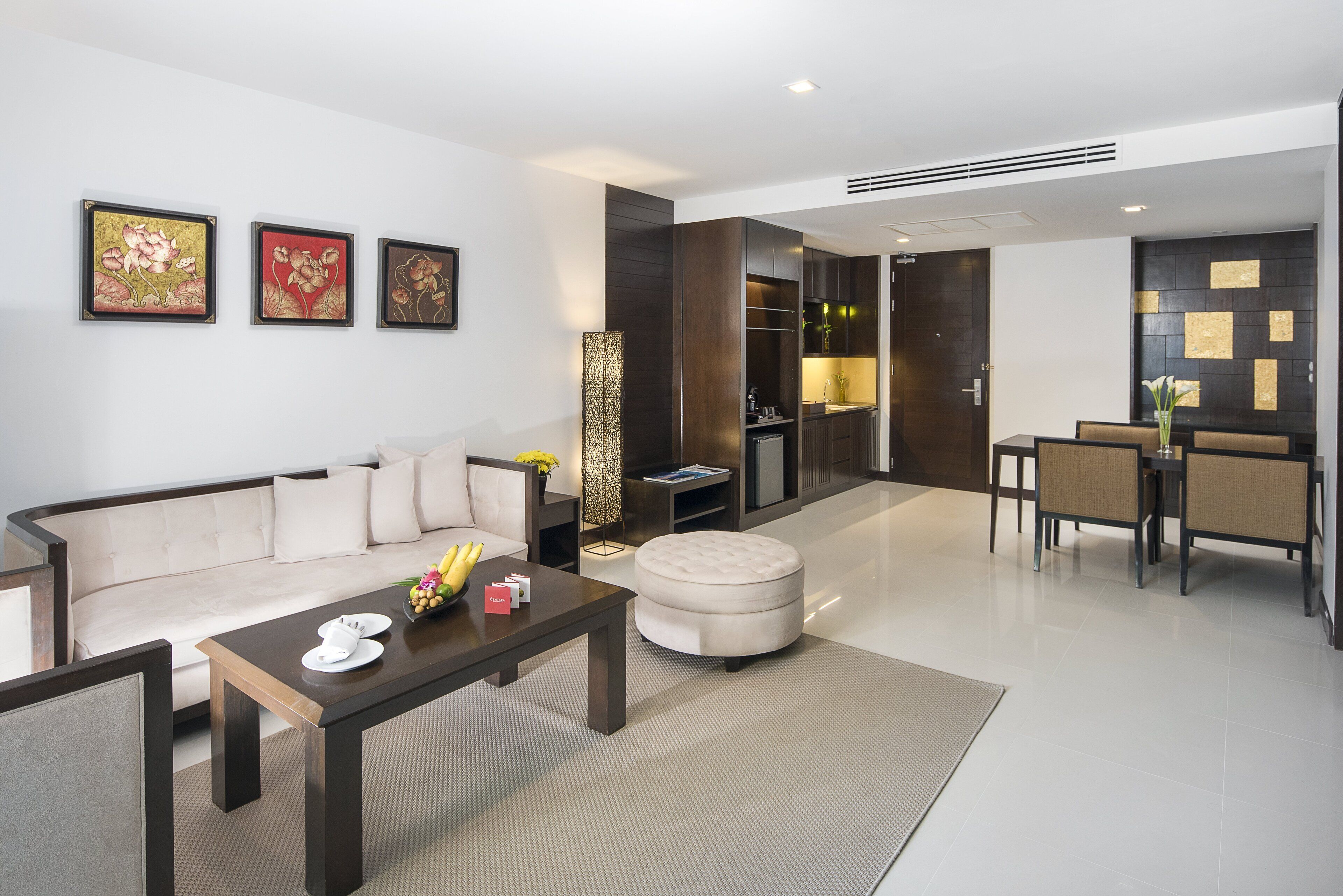 A modern living room with a sofa, coffee table, and dining area. There are framed artworks on the wall and a tall decorative column.