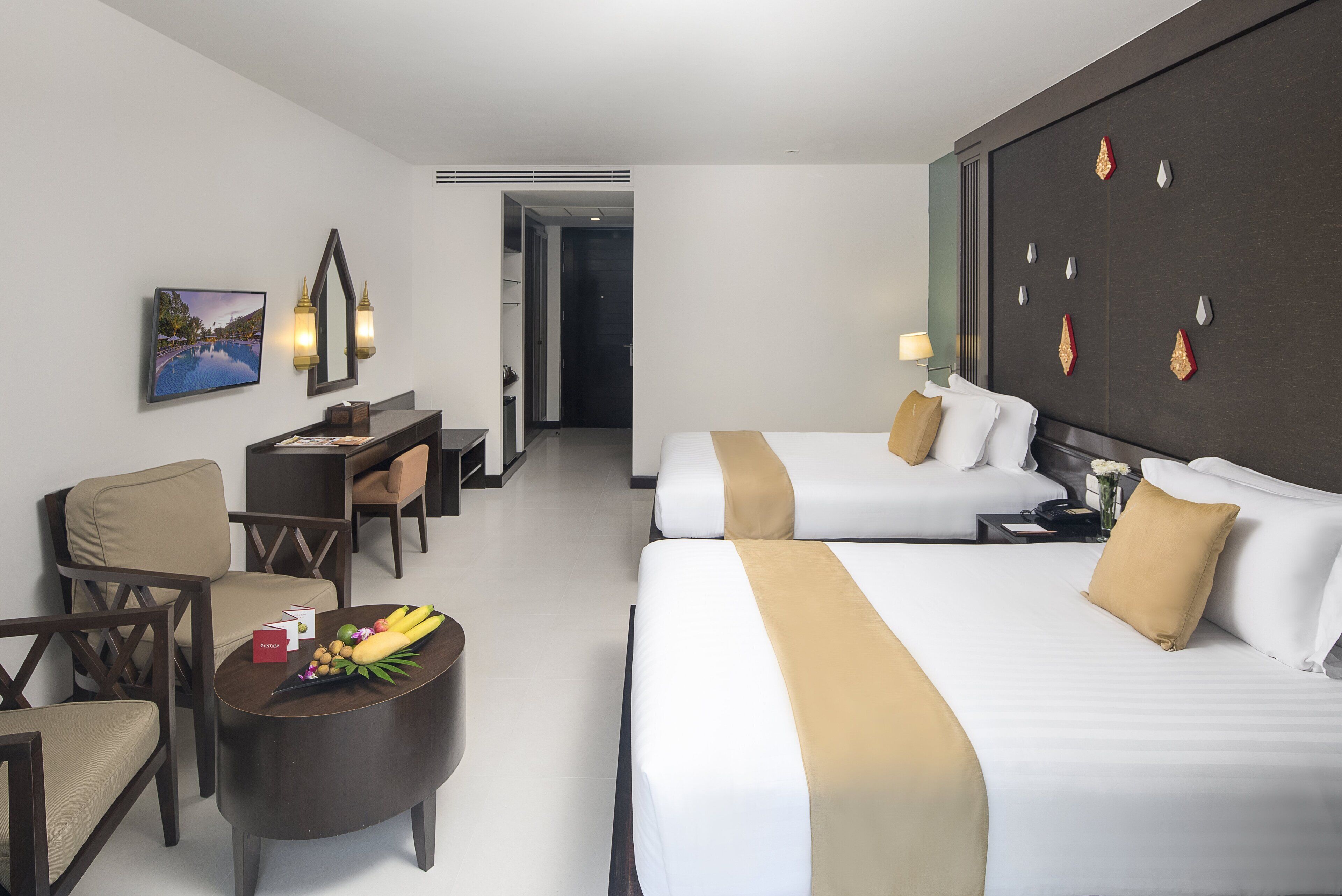 Habitación de hotel con dos camas, un escritorio, una silla y una mesa de centro con fruta.