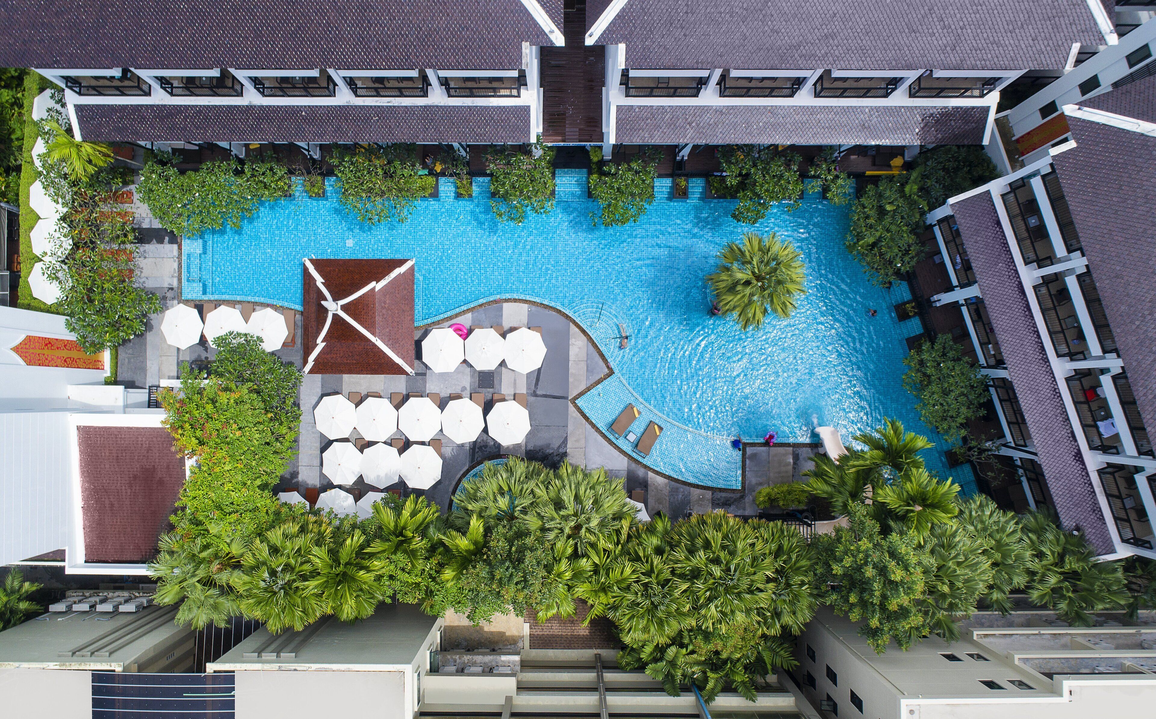 Vista aérea de un hotel con piscina rodeada de palmeras y mobiliario para exteriores.