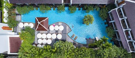 Vista aérea de un hotel con piscina rodeada de palmeras y mobiliario para exteriores.