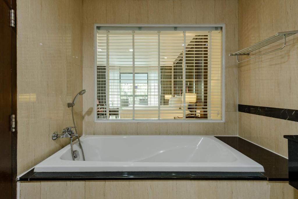 Een moderne badkamer met een groot bad, een raam met zonwering en een handdoekrek.