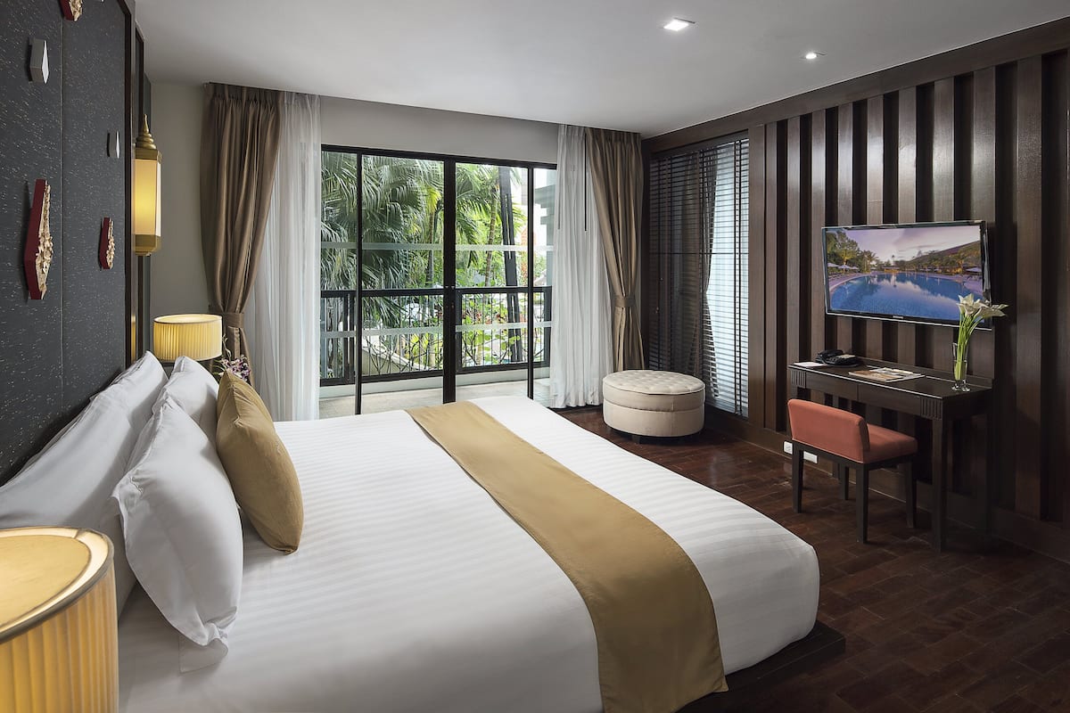 Une chambre d’hôtel moderne dotée d’un grand lit, d’un bureau avec une chaise, d’une télévision et offrant une vue sur la verdure par la fenêtre.