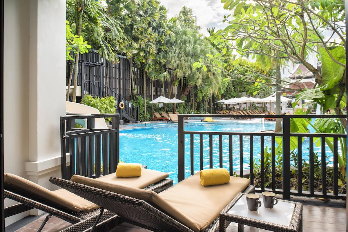 Un espace aménagé au bord de la piscine, avec des chaises longues et des parasols, entouré d’une végétation luxuriante.
