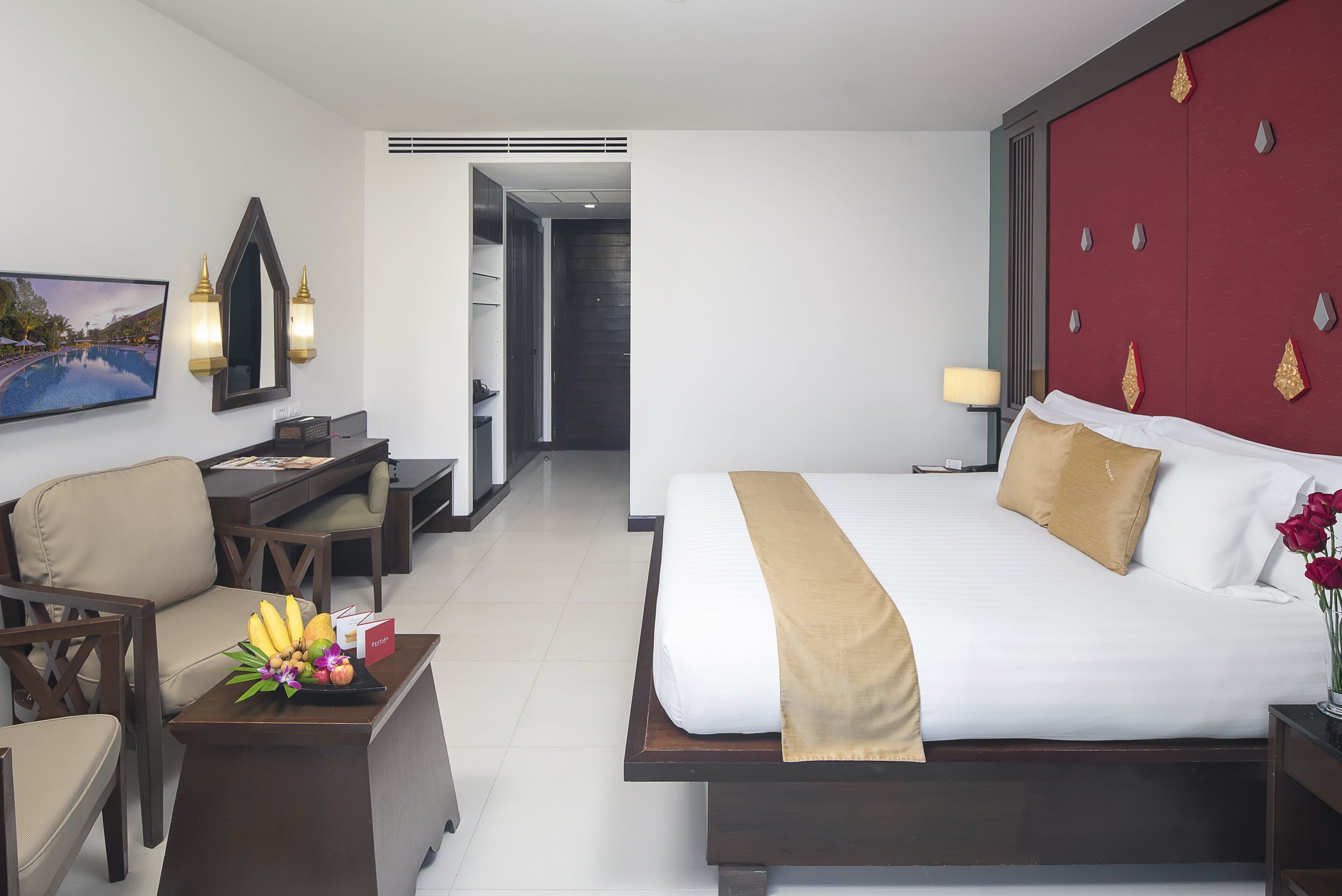 A hotel room with a bed, a desk, and a chair. There is a painting on the wall and a vase with flowers on the desk.