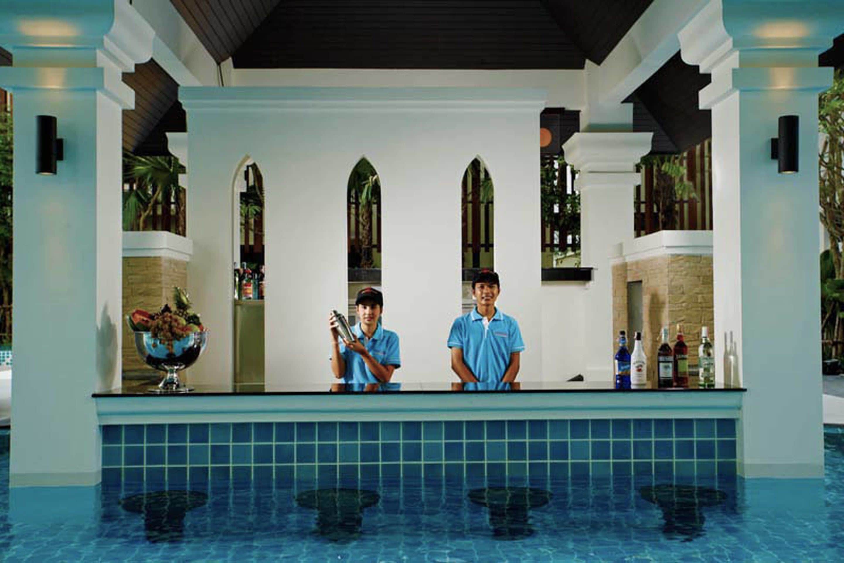 Eine Poolbar mit zwei Mitarbeitern, einem gefliesten Pool und einer Steinwand.
