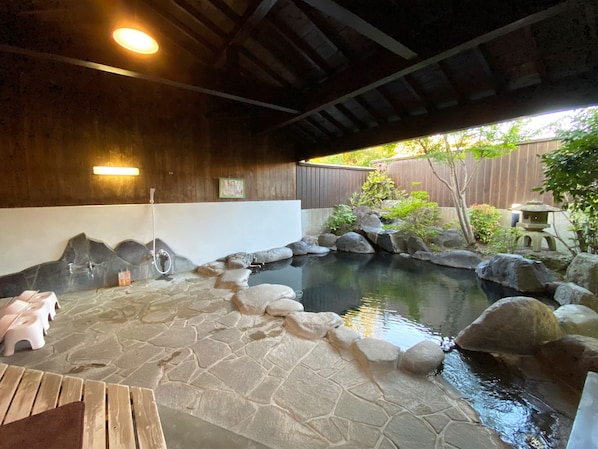 A stone-tiled hot tub area with a wooden ceiling, a small waterfall feature, and a wooden deck with pink stools.