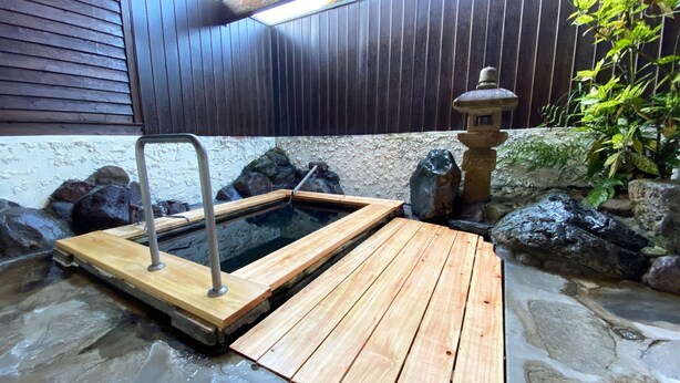 Area termale con gradini di legno che conducono all'acqua, circondata da rocce e una recinzione in legno.