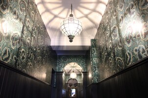 A hallway with ornate wallpaper and a hanging light fixture.