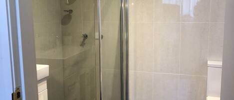Un baño moderno con ducha de vidrio, inodoro blanco y lavabo con encimera blanca.