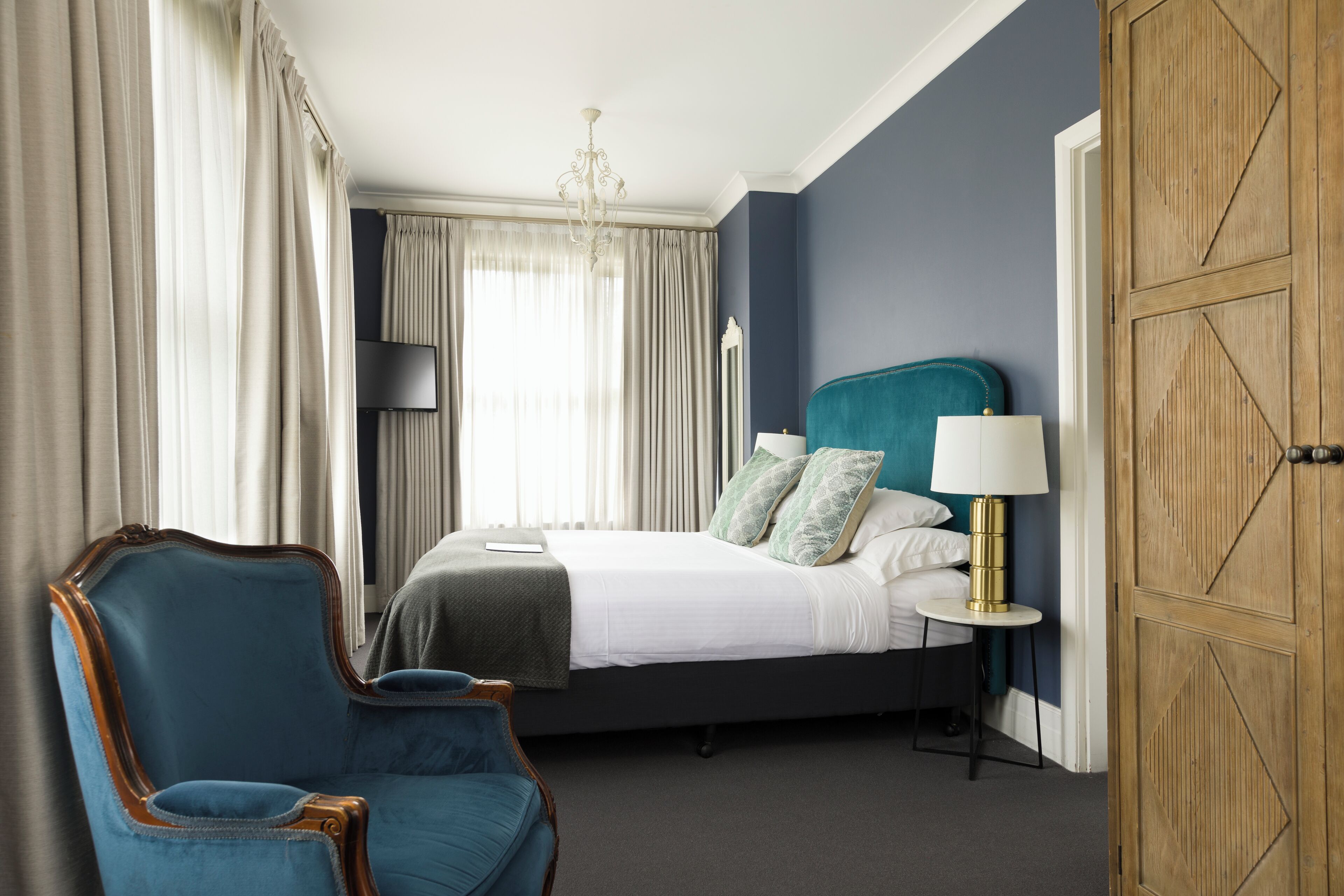 A hotel room with a bed, a chair, a lamp, and a wardrobe.