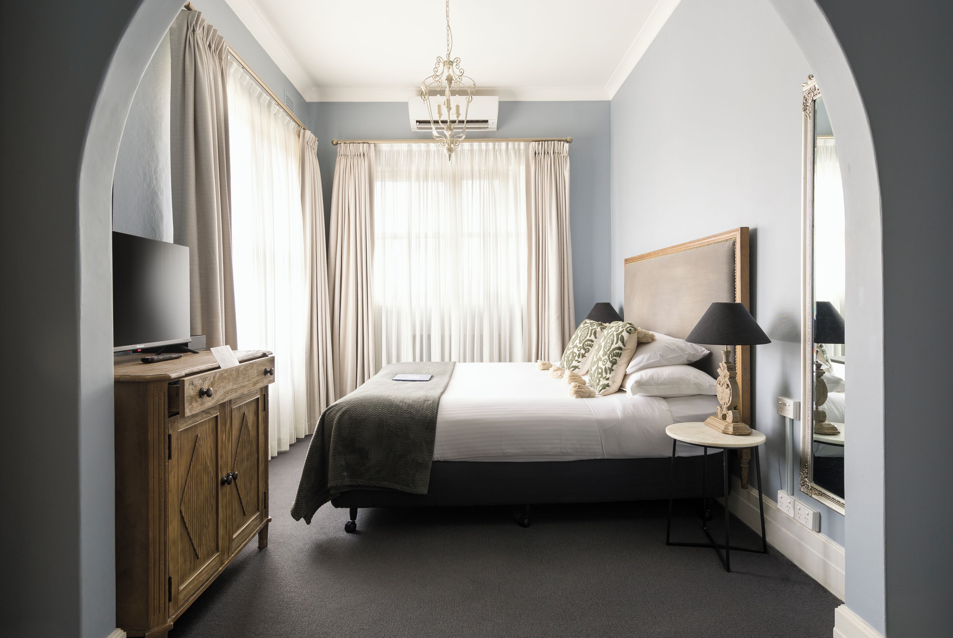 A bedroom with a bed, bedside table, lamp, wardrobe, and a large mirror.