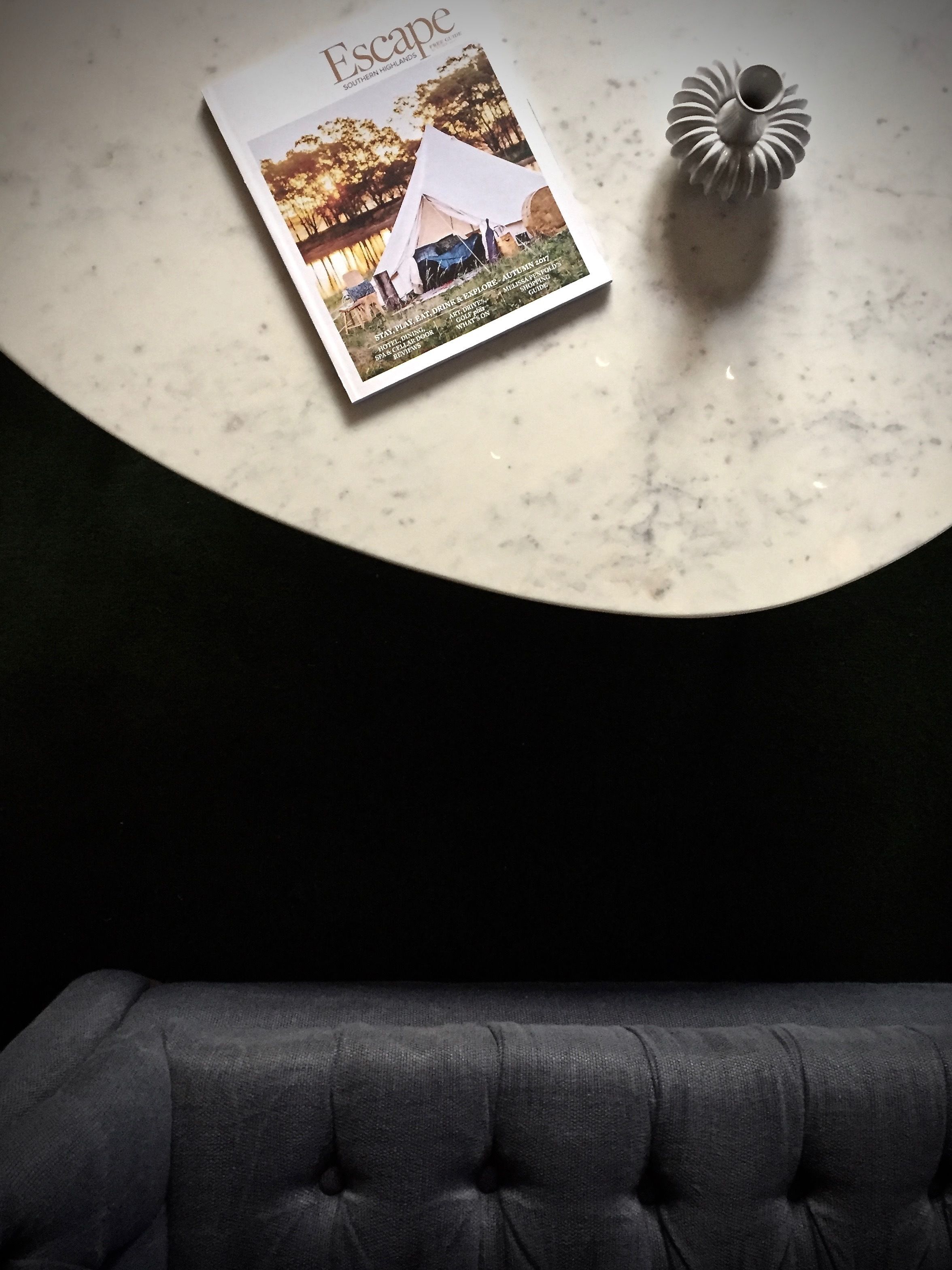 A magazine titled 'Escape' on a marble table with a cushion in the foreground.