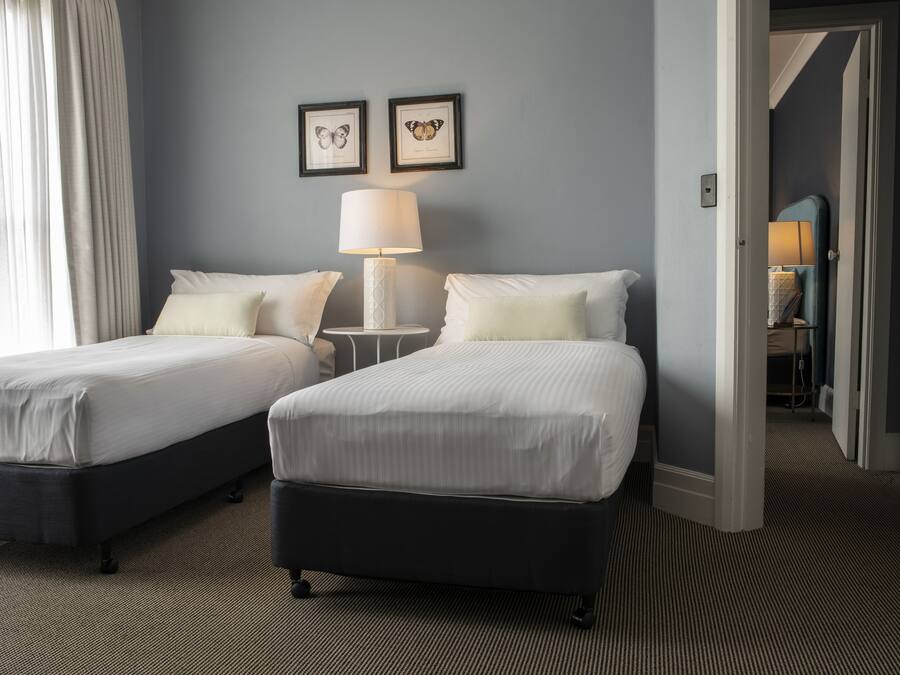 A hotel room with two beds, a nightstand with a lamp, and a door leading to another room.