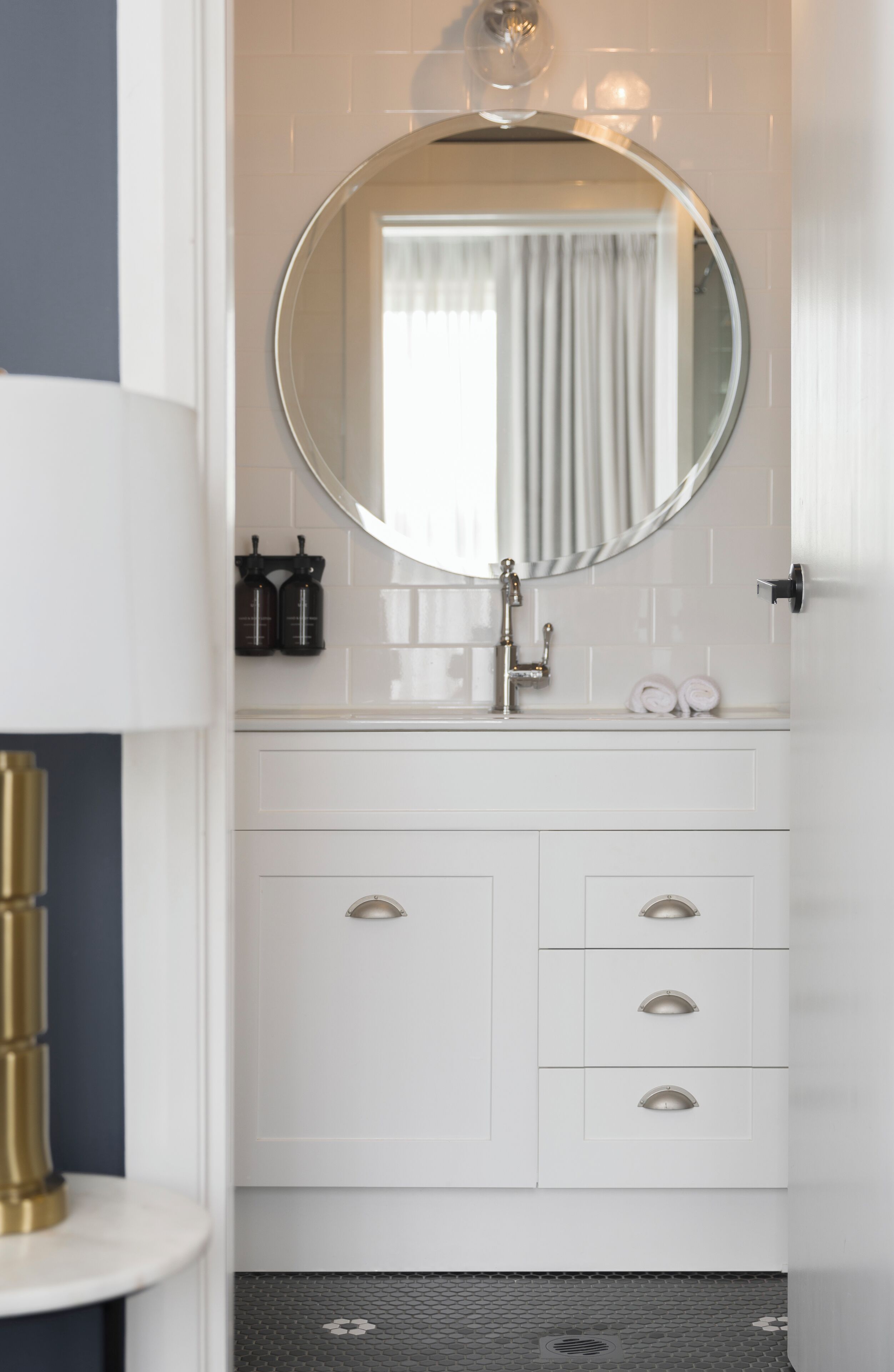 A bathroom with a white vanity, a round mirror, and a towel rack.