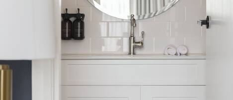 Une salle de bain avec un meuble-lavabo blanc, un miroir rond et un porte-serviettes.
