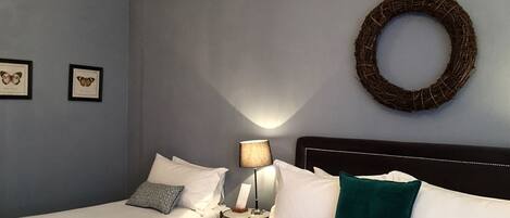 Habitación de hotel con dos camas individuales, una mesita de noche con lámpara, un arreglo en la pared y dos cuadros con mariposas.