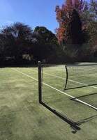 Una cancha de tenis con red, rodeada de árboles y una valla.