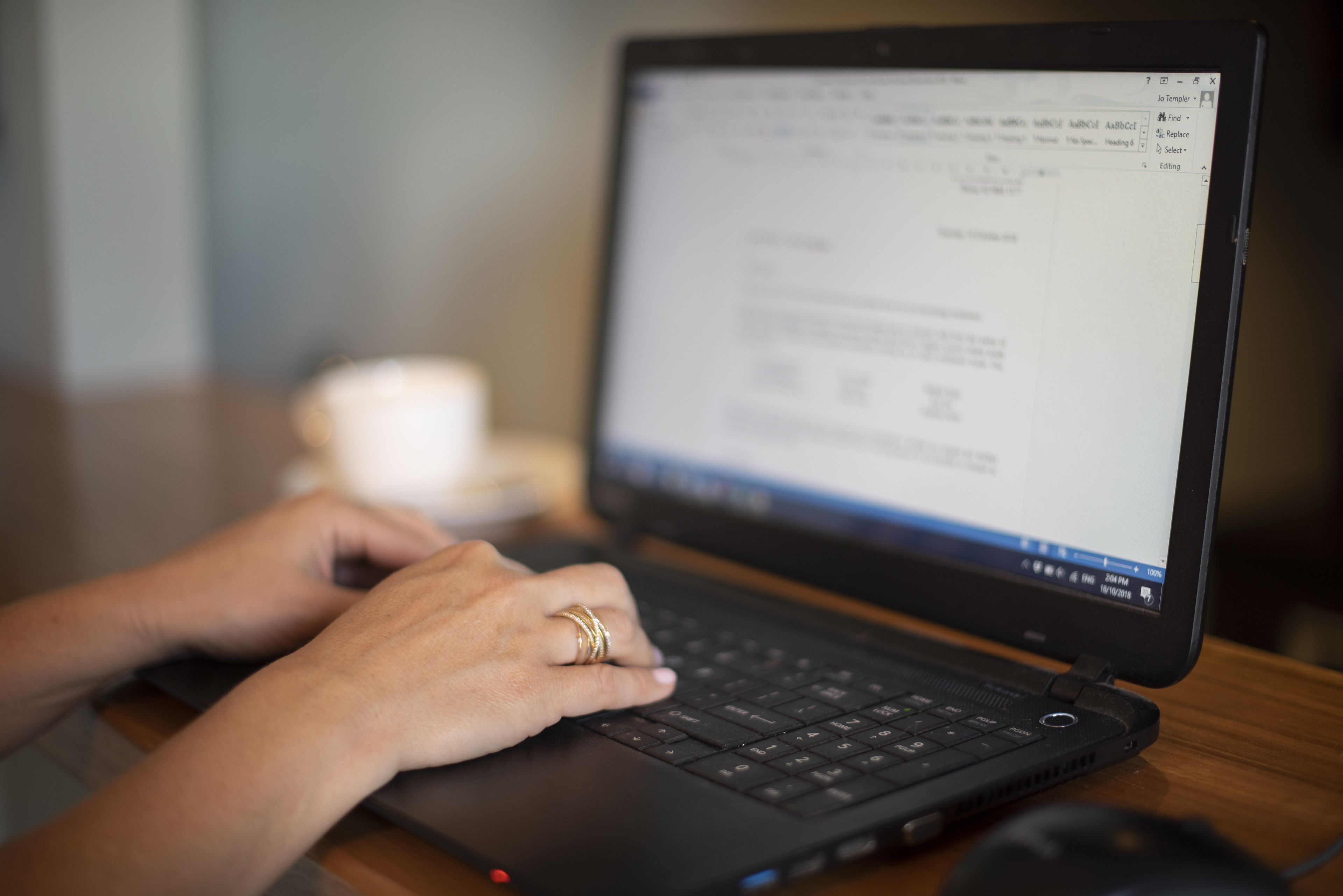 A laptop on a wooden desk with a person typing.