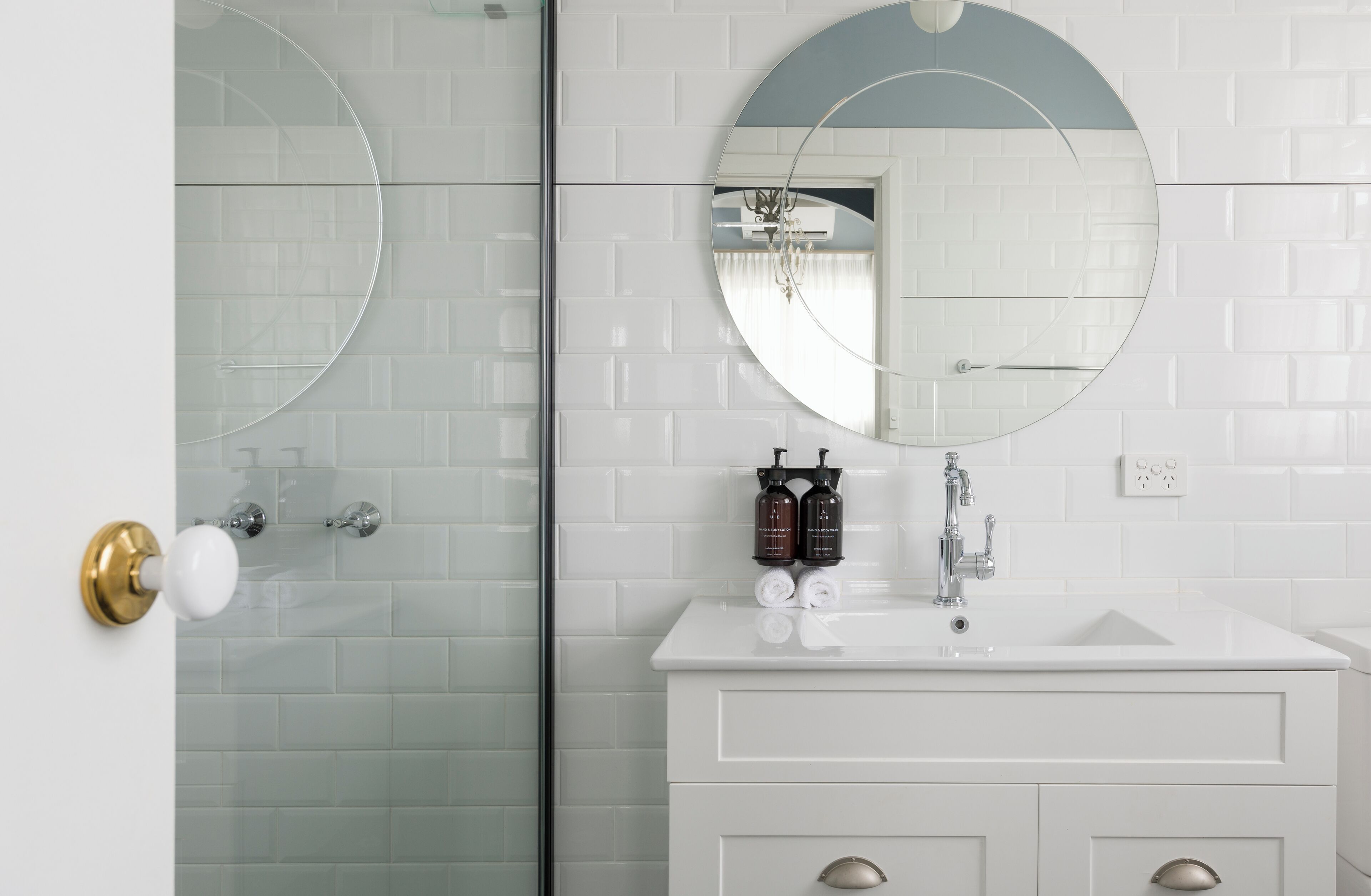 A bathroom with a white vanity, a round mirror, and a glass shower enclosure.
