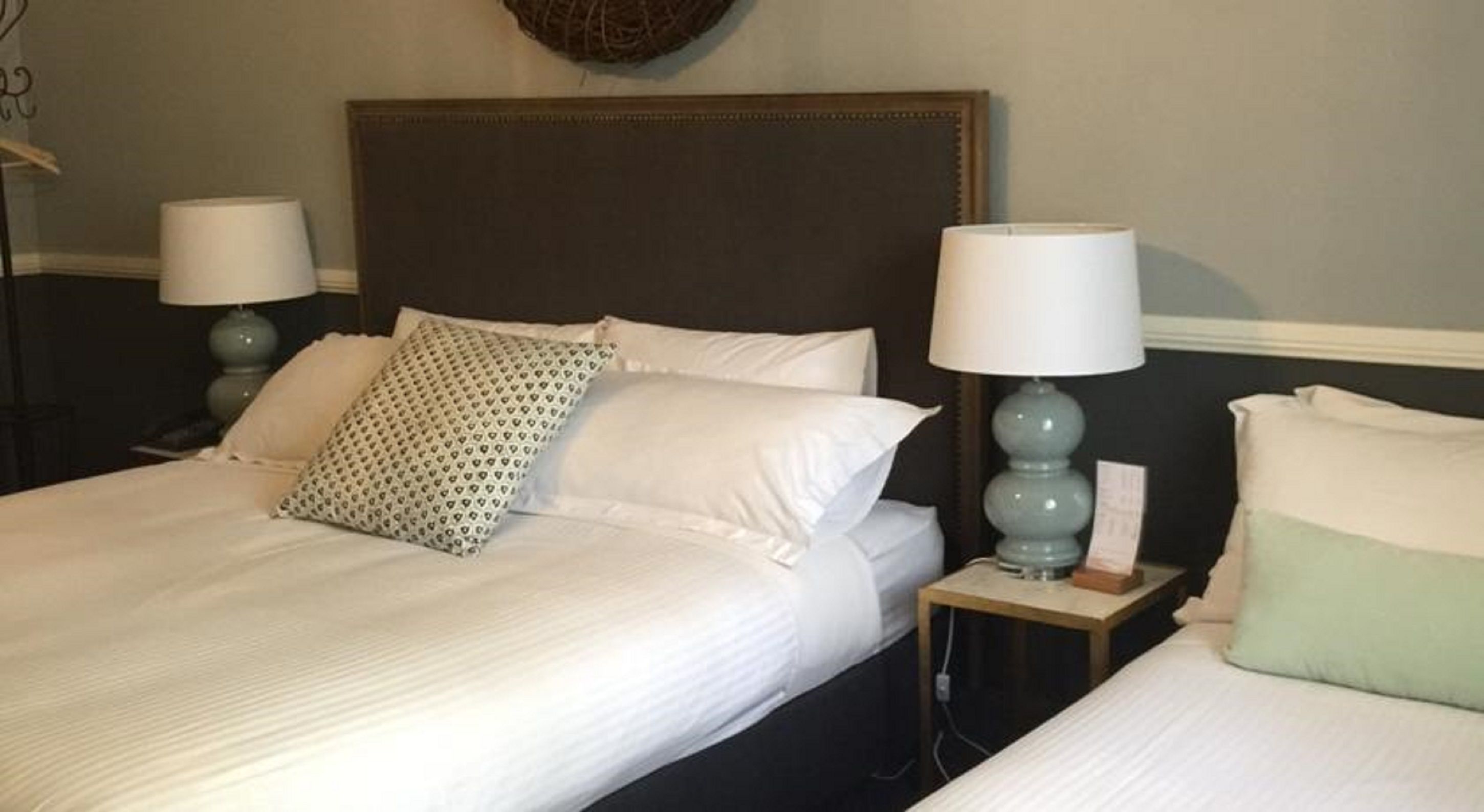 A hotel room with two beds, each with a white bedspread and pillows, a dark headboard, and two bedside lamps.