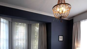 Une chambre d’hôtel avec un grand lit, deux fauteuils, une table avec une bouteille et des verres, un lustre et un radiateur.