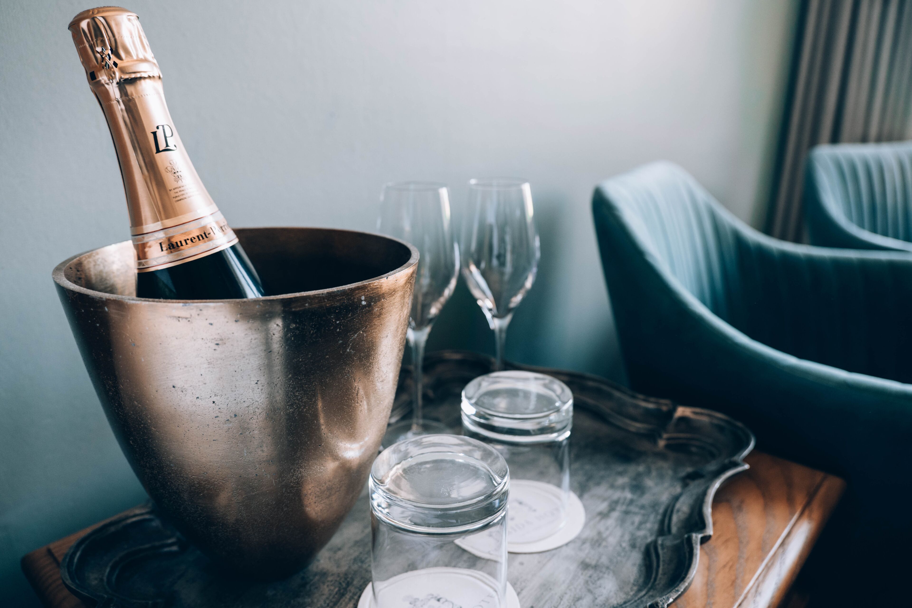 A champagne bottle in a copper bucket, two empty wine glasses, and a tray on a table.