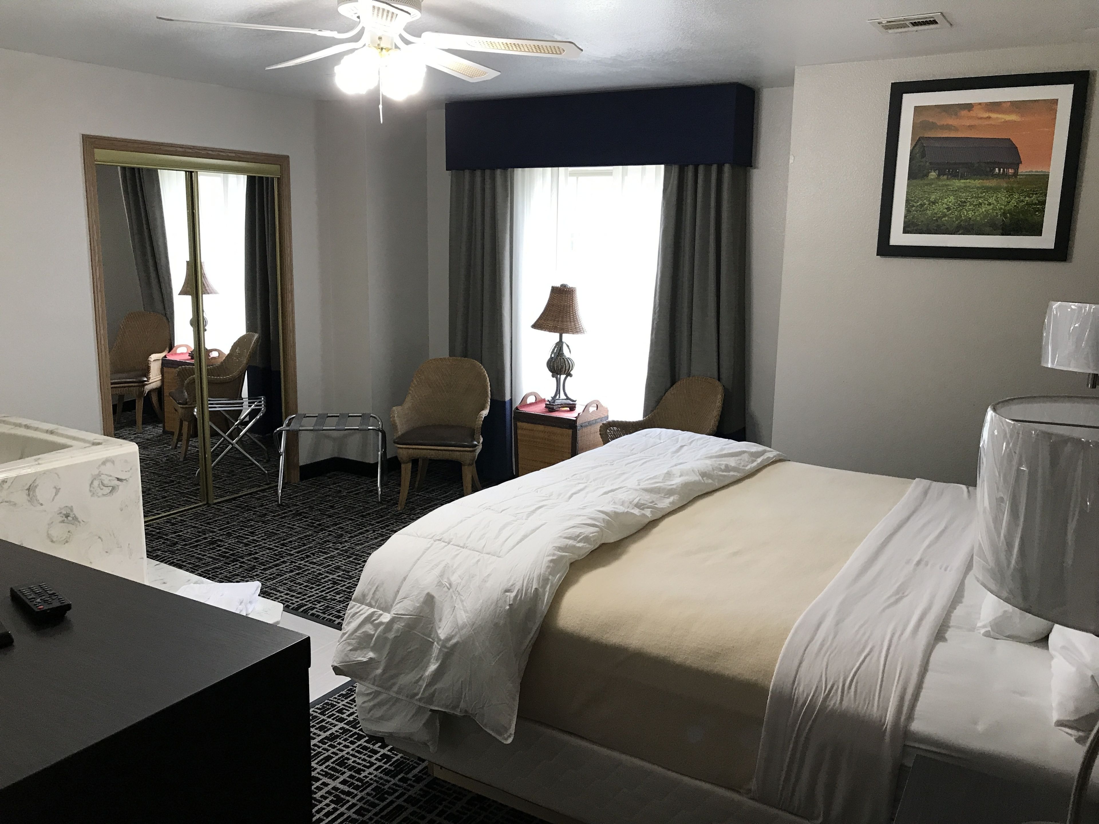 A hotel room with a bed, a desk, a chair, a small table, a lamp, and a picture on the wall.