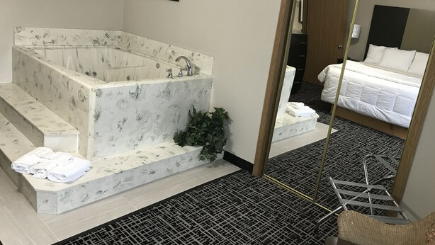 A modern bathroom with a freestanding bathtub, a large mirror, and a neatly made bed.