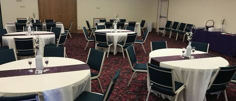 A banquet hall with round tables, chairs, and a red carpeted floor.