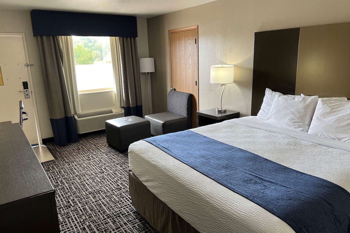 A hotel room with a large bed, a desk, a chair, a lamp, and a window with curtains.
