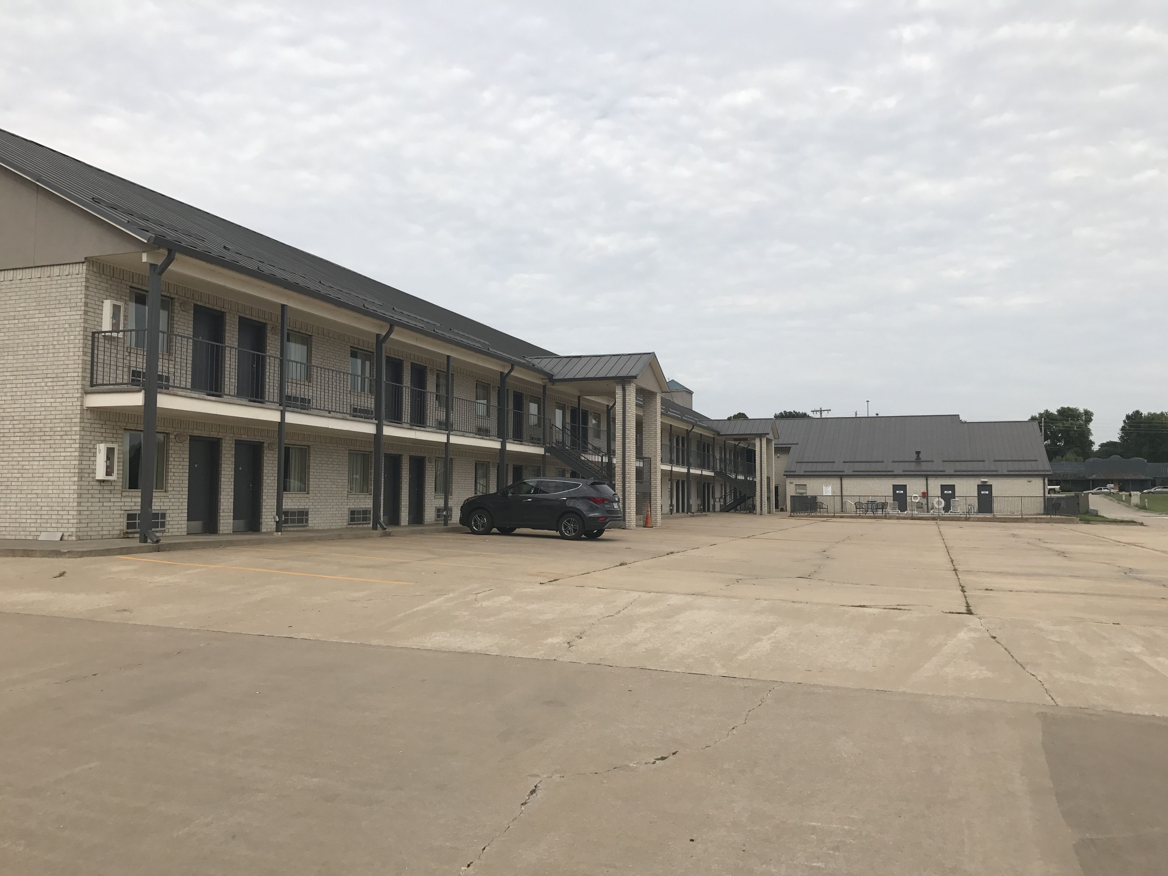 Een motel met meerdere verdiepingen, een parkeerplaats en een klein gebouw met een bord.
