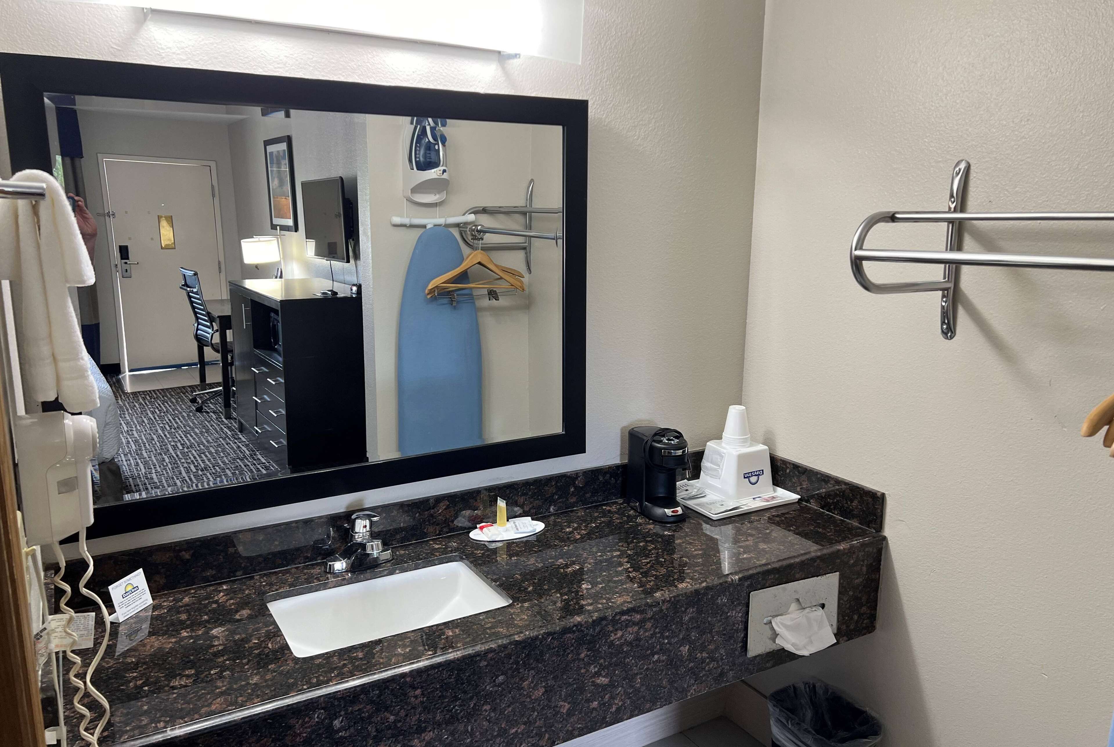 A hotel bathroom with a large mirror, a sink, a towel rack, a coffee maker, and a trash bin.