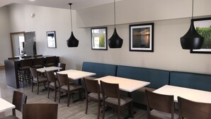 A modern dining area with tables and chairs, a blue booth, and pendant lighting.