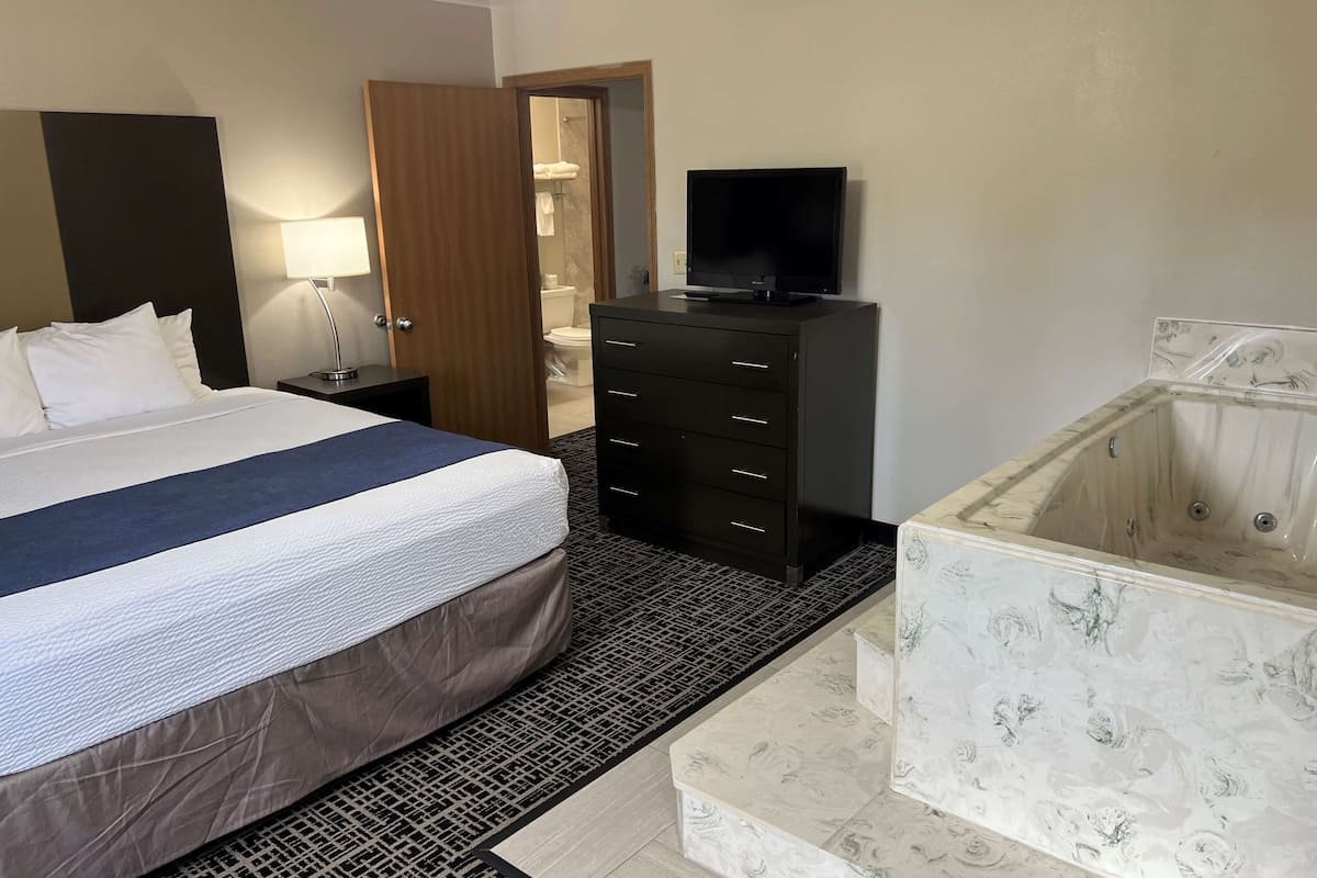 A hotel room with a bed, a TV, a dresser, a bathroom with a bathtub, and a patterned floor.
