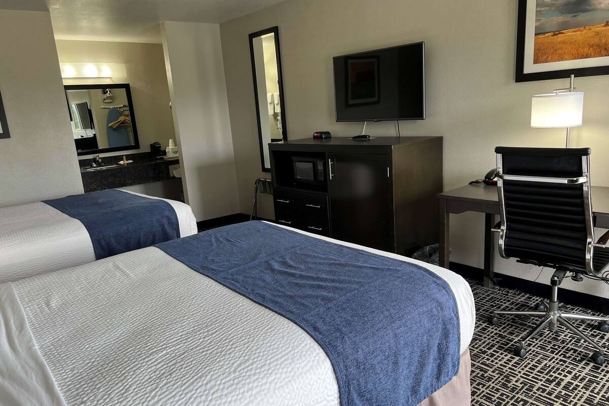 A hotel room with two beds, a desk with a chair, a TV, and a mirror.