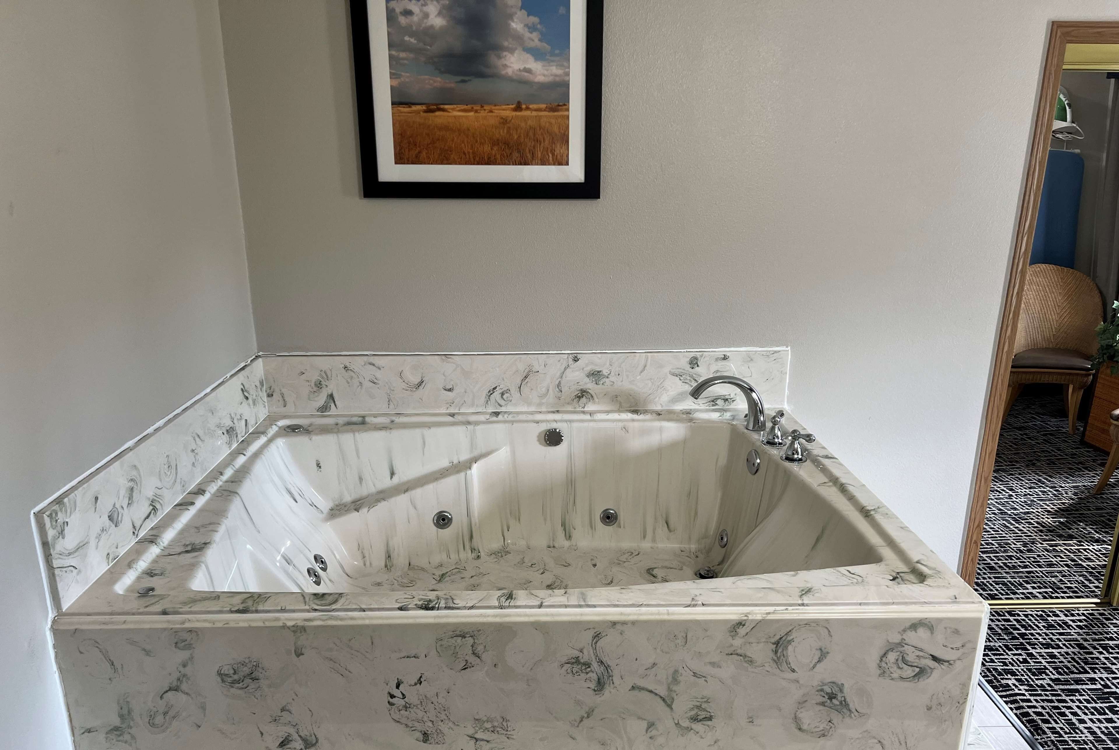 A rectangular bathtub with a marble pattern, a framed picture above it, and a chair in the background.