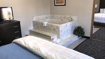 A hotel room with a bed, a black dresser, a marble bathtub, and a framed picture on the wall.