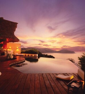 A wooden deck with a lounge chair and a thatched-roof structure, overlooking a calm body of water and distant mountains during sunset. - Tentaciones Hotel & Lounge Pool - Adults Only (Zihuatanejo)