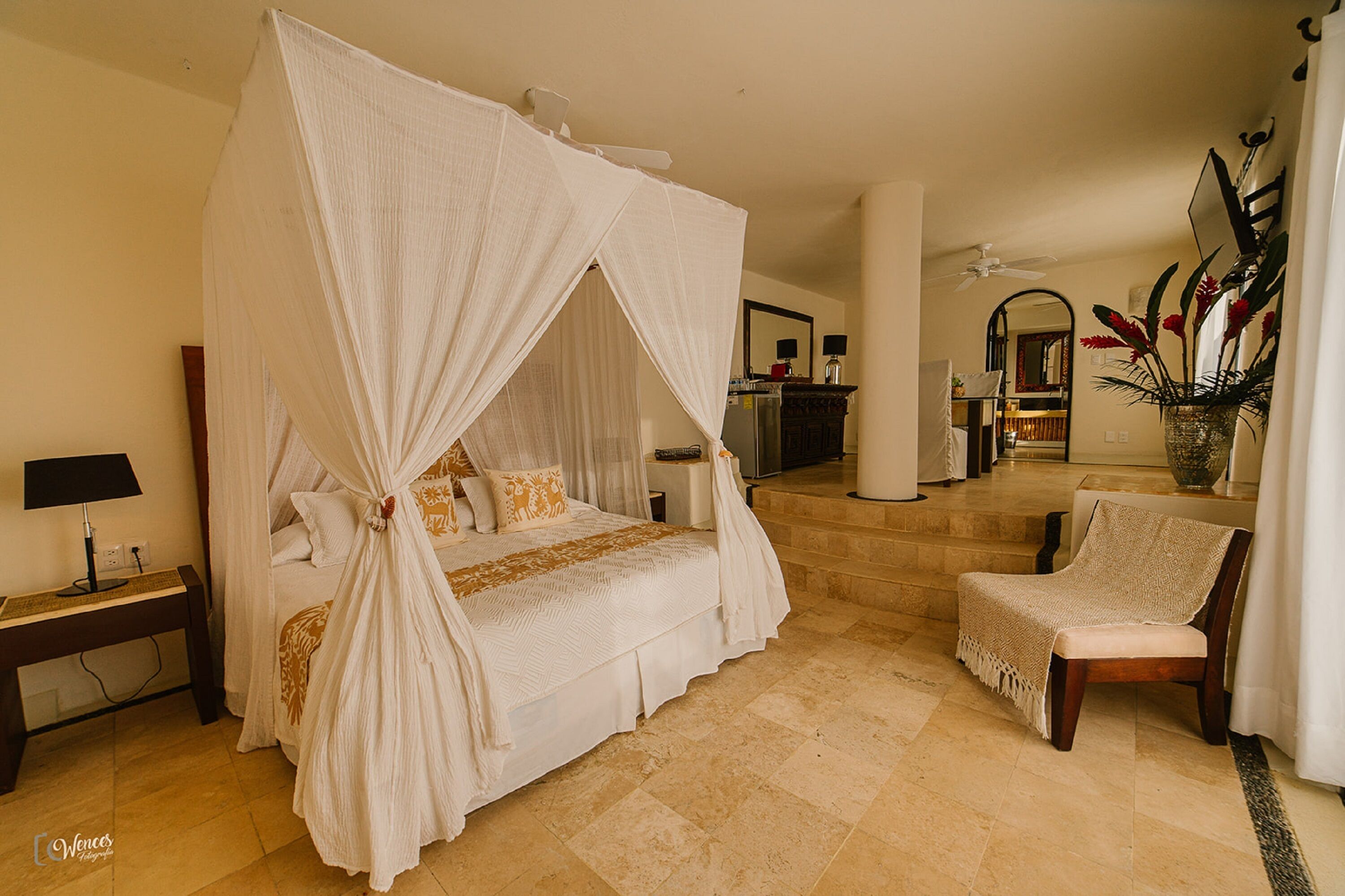 Un espacioso dormitorio con cama con dosel, una zona de estar con una silla y vistas al salón.