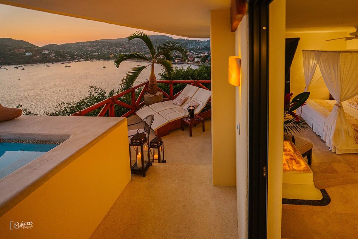 Un balcón con piscina, una cama con dosel y vistas al mar.