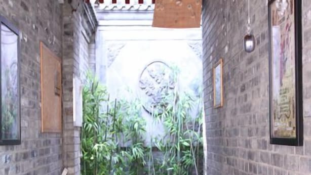 Un étroit couloir en briques, orné de tableaux encadrés, mène à un espace aménagé en jardin de bambous.
